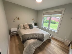 A bedroom with a bed, a window, a radiator, and a wall-mounted light fixture. - Luxury Lakefront | Golf Sim & Theatre | Dock (Westport)
