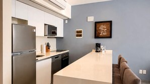 A modern kitchen with a central island, stainless steel appliances, and a blue accent wall. - Quiet Pool-View 1BR Near 5th Avenue (Playa del Carmen)