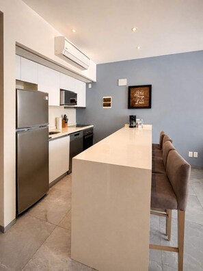A modern kitchen with a central island, stainless steel appliances, and a blue accent wall. - Quiet Pool-View 1BR Near 5th Avenue (Playa del Carmen)