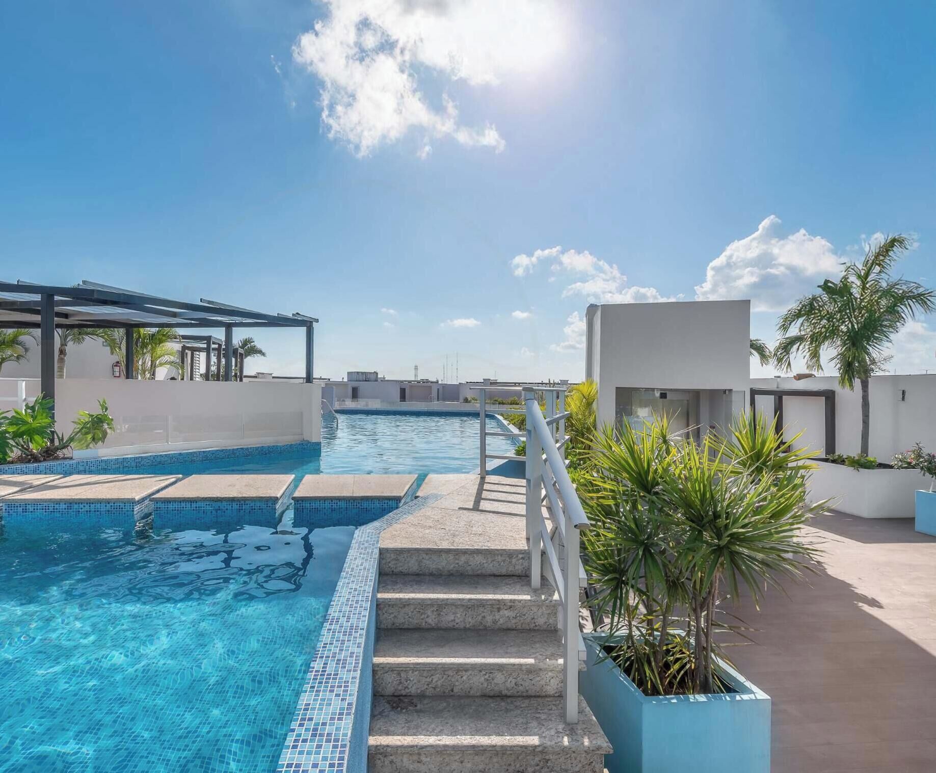 Une piscine sur le toit avec une eau d’un bleu cristallin, un espace salon couvert et un bâtiment moderne en arrière-plan.