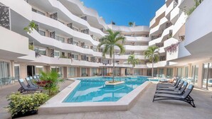 A multi-level hotel with a central swimming pool, balconies with plants, and outdoor seating areas. - Quiet Pool-View 1BR Near 5th Avenue (Playa del Carmen)