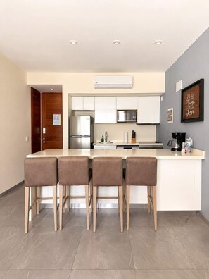 A modern kitchen with a central island, bar stools, stainless steel appliances, and a wall-mounted air conditioner. - Quiet Pool-View 1BR Near 5th Avenue (Playa del Carmen)