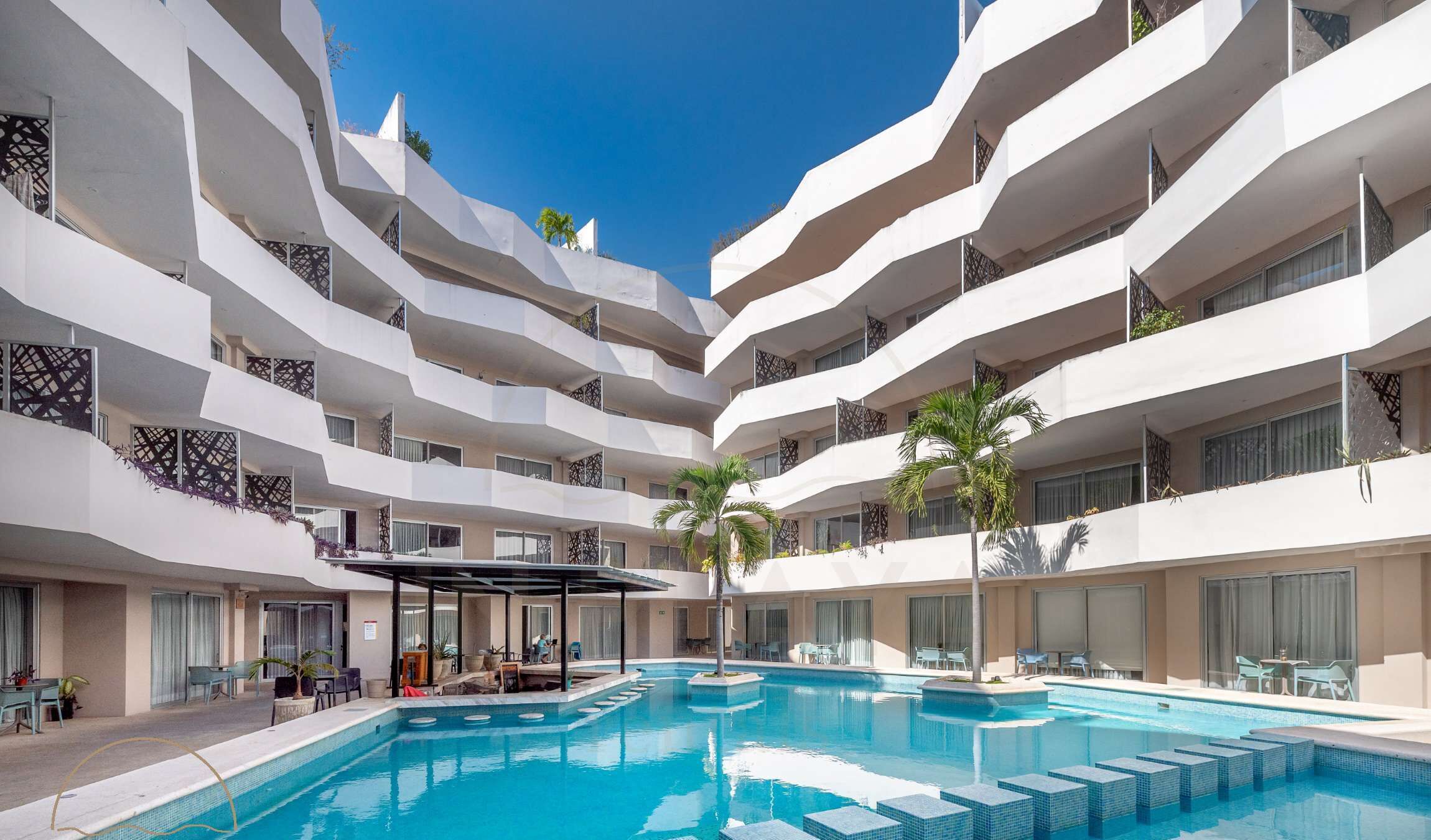 Ein mehrstöckiges Hotel mit einem zentralen Schwimmbecken, Balkonen mit Geländern und Außenbereichen zum Sitzen.