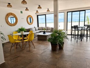 Ein großzügiger Wohnbereich mit einer Couch, gelben Stühlen, einem Couchtisch und großen Fenstern mit Blick auf den Himmel und die weite Landschaft.