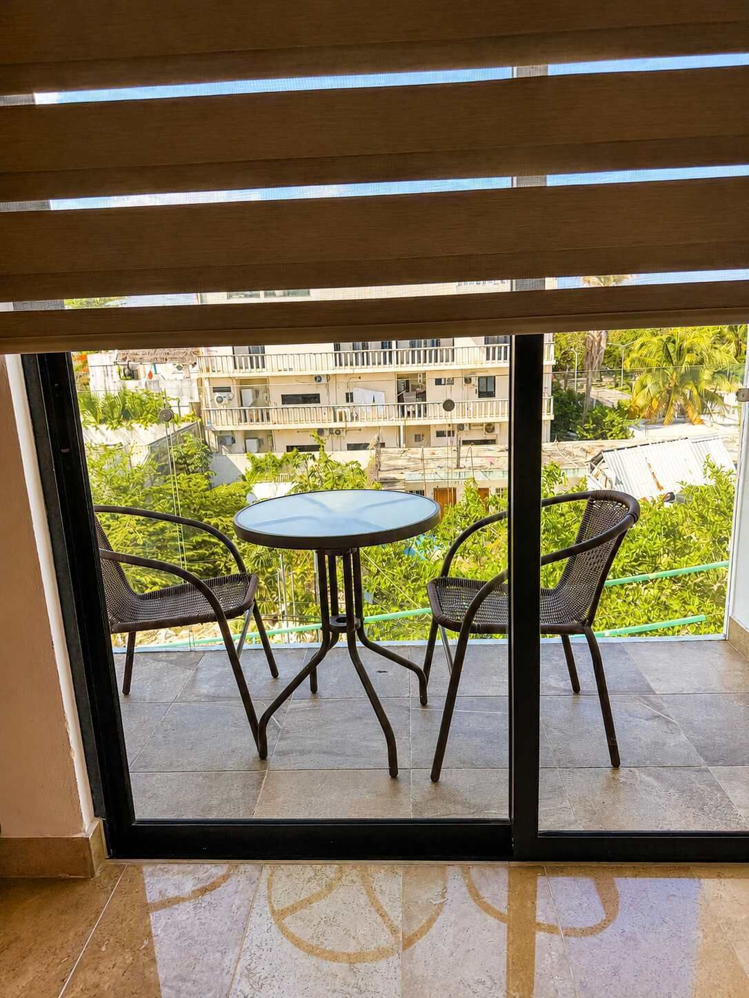 Un balcón con mesa y sillas, vista hacia una zona residencial y un edificio con balcones.