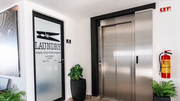 Entrada de um hotel com uma porta de vidro fosco identificada com 'LAUNDRY' e um extintor de incêndio fixado na parede.
