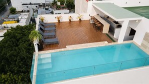 Ein Pool auf dem Dach mit Holzterrasse, Liegestühlen und Bar.