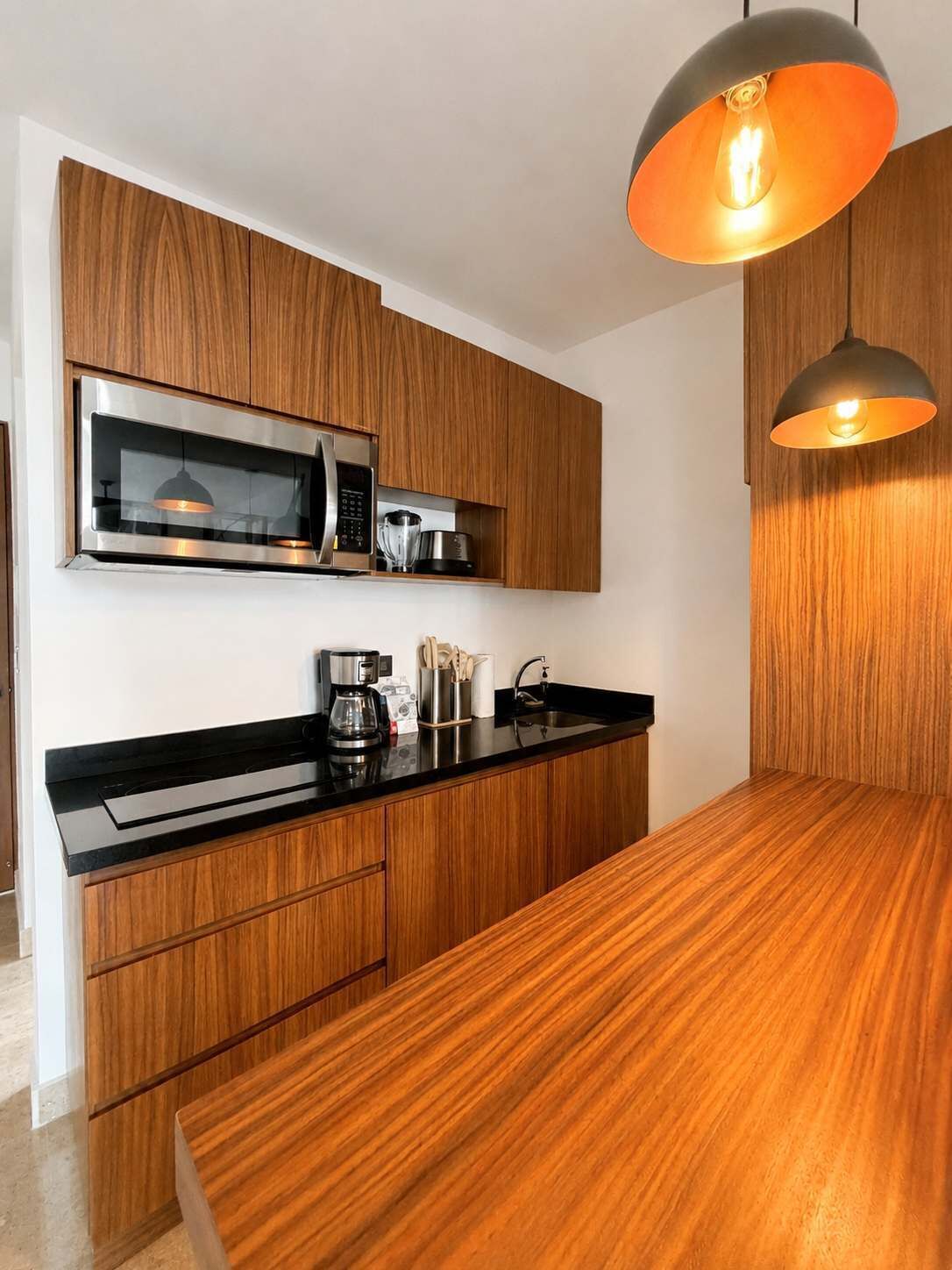 A modern kitchen with wooden cabinetry, a black countertop, and a hanging pendant light.