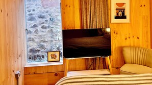 Une chambre à coucher avec un lit, un téléviseur posé sur un meuble, une fenêtre donnant sur des rochers et des murs en bois.