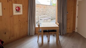 Une pièce avec un plancher en bois, une table entourée de chaises, une fenêtre avec des rideaux et une porte.
