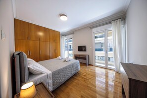 Ein Schlafzimmer mit Bett, Holzschrank, Schreibtisch, Fernseher und Balkonblick.