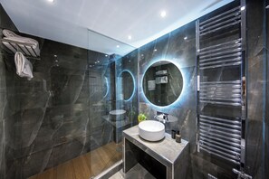 Un baño moderno con ducha de vidrio, espejo redondo y lavamanos integrado.