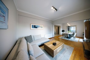 A modern living room with a sectional sofa, a wooden coffee table, and a dining area with a round table and chairs. - Elenas Luxury Apartment/Panoramic Acropolis View (Athina)