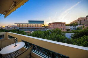 A balcony with a table and chairs, overlooking a cityscape with modern and historic buildings. - Elenas Luxury Apartment/Panoramic Acropolis View (Athina)