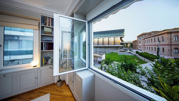 A room with a large window, a bookshelf, and a radiator. - Elenas Luxury Apartment/Panoramic Acropolis View (Athina)