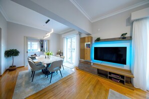 Una sala de estar moderna con comedor, televisor de pantalla plana, piso de madera y un gran ventanal.
