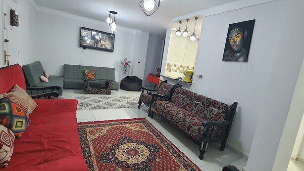 A living room with a red sofa, a patterned sofa, a coffee table, a TV mounted on the wall, and a patterned rug. - One Minute To The Sea-Asafra Beach 
Fast WiFi - AC - Family Friendly (Alexandria Governorate)
