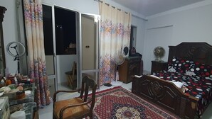 A bedroom with a wooden bed, a chair, a small table, and a window with curtains. - One Minute To The Sea-Asafra Beach 
Fast WiFi - AC - Family Friendly (Alexandria Governorate)