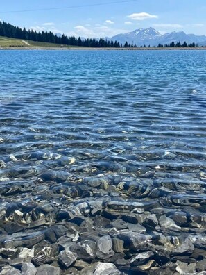 A lake with clear water, rocky shore, and a mountain range in the background. - Hostcare - Le Coeur Blanc – Les Saisies Centre (Hauteluce)