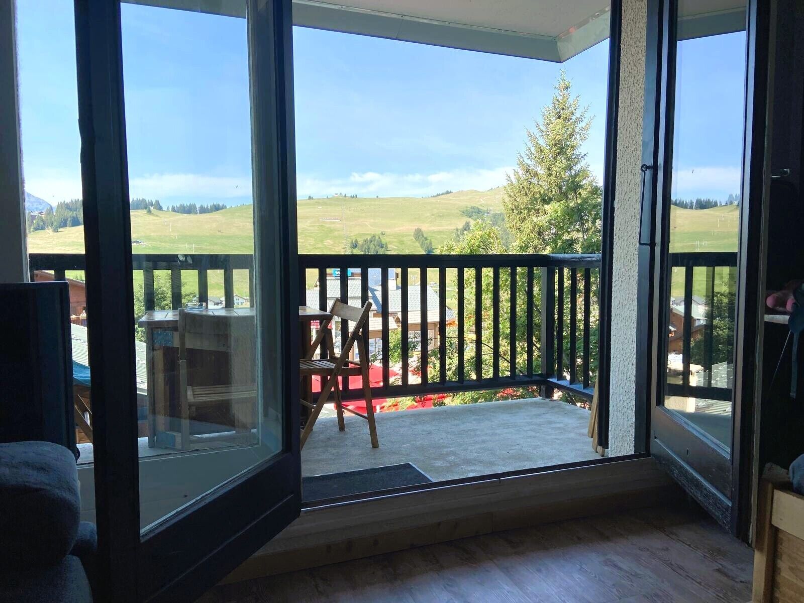 Una habitación con puerta de cristal que da a un balcón con vistas a un paisaje verde y un árbol.