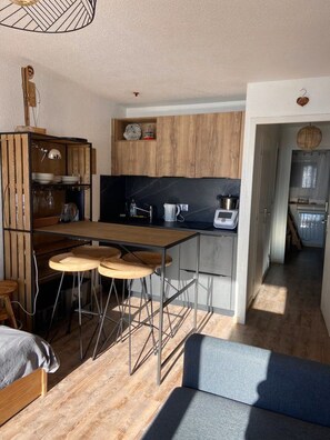Een kleine keuken met een houten tafel, barkrukken en een moderne kookplaat.