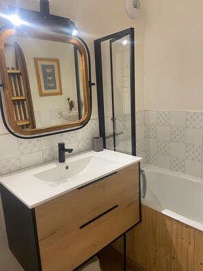 Ein Badezimmer mit einem weißen Waschbecken, einer Holz-Kommode, einem großen Spiegel und einer Badewanne.