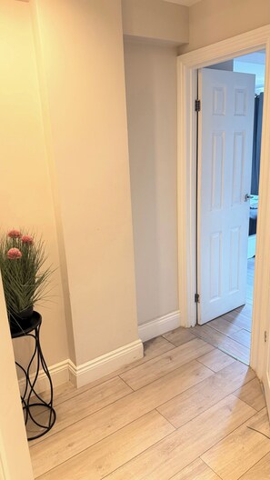 A hallway with a white door, a potted plant, and wooden flooring. - Marble Arch Elevator Ac - 3 Bedroom Apartment (London)