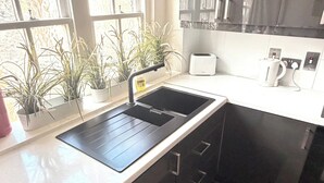 A modern kitchen with a built-in stove, a sink, and a countertop. There are potted plants on the windowsill and a coffee maker on the counter. - Marble Arch Elevator Ac - 3 Bedroom Apartment (London)