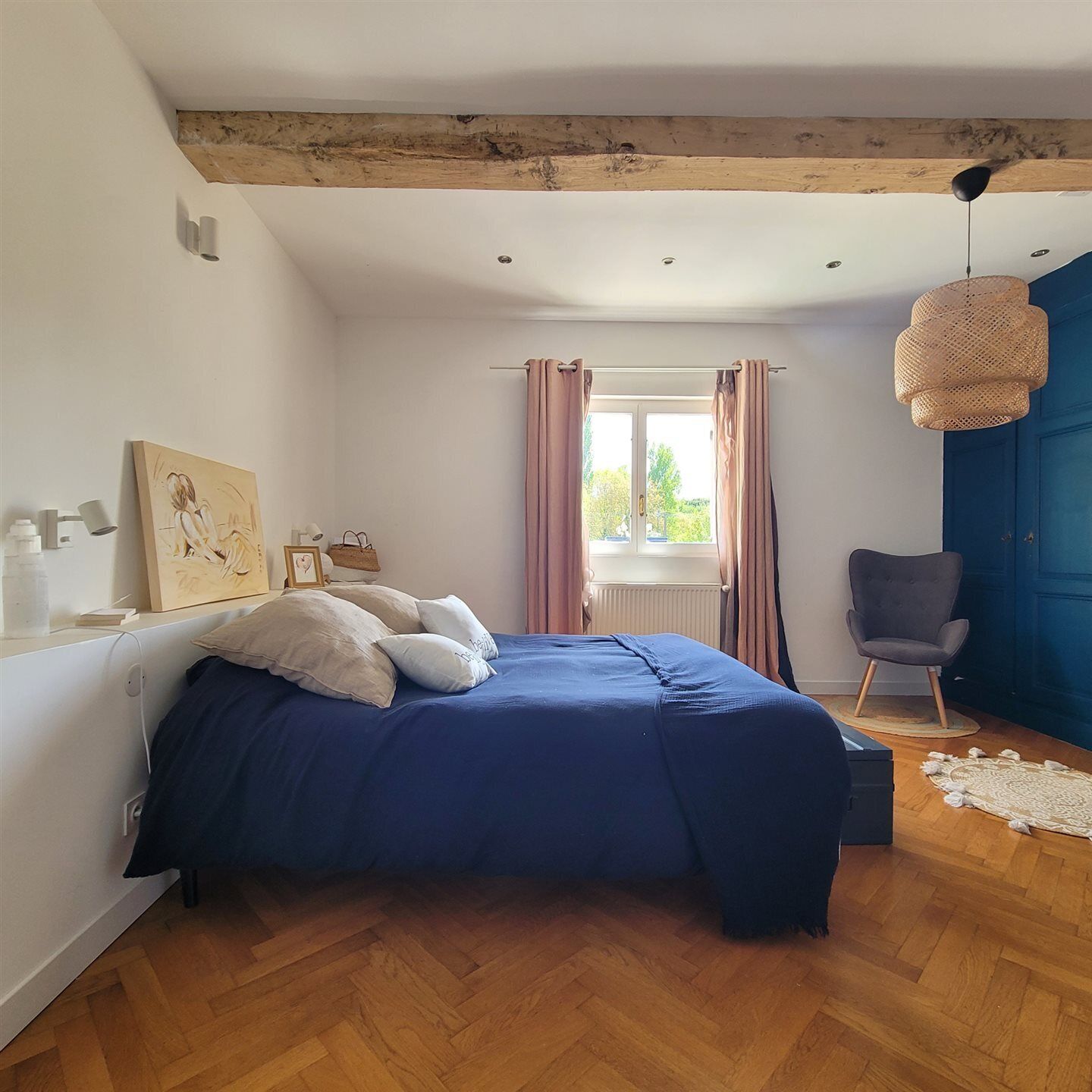 A bedroom with a bed, a chair, a window with curtains, a hanging light, and a wooden ceiling.