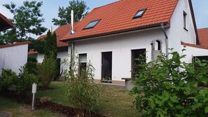 A white building with a red-tiled roof, a chimney, and a small window. - Familienfreundliches Ferienhaus mit Garten im Hafendorf Muritz (Rechlin)