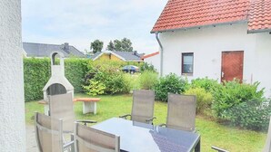 A patio with a table and chairs, a barbecue grill, and a car parked in the background. - Familienfreundliches Ferienhaus mit Garten im Hafendorf Muritz (Rechlin)