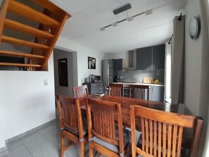 A dining area with a wooden table and chairs, a kitchen with modern appliances, and a staircase leading to an upper level. - Familienfreundliches Ferienhaus mit Garten im Hafendorf Muritz (Rechlin)