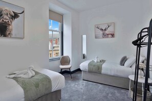 Une chambre d’hôtel avec deux lits, une chaise, une fenêtre donnant sur des immeubles et des œuvres d’art accrochées aux murs.