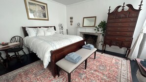 A bedroom with a large bed, a bench, a dresser, a chair, a fireplace, and a mirror. - Lilac Inn Waddington (Waddington)