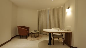 Une chambre d’hôtel de taille réduite, comprenant une table à manger, deux chaises, une petite table d’appoint et un fauteuil.