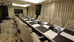 Une salle de conférence avec une longue table, des chaises, un téléviseur à écran plat et un sol recouvert de moquette.