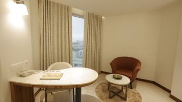 Habitación de hotel con una mesa de comedor, una mesita auxiliar, un sillón rojo y vista a la ciudad desde la ventana.