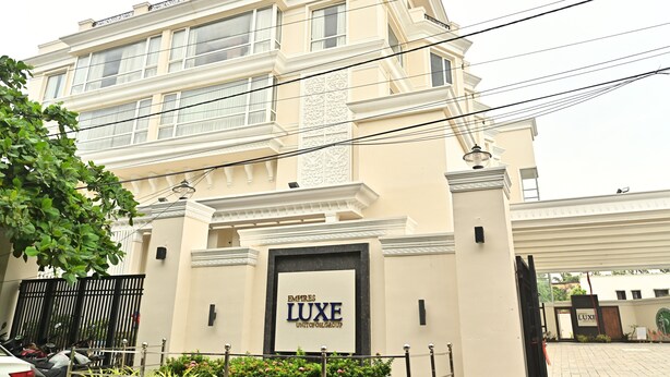 Un hôtel à plusieurs étages, doté d’une entrée imposante, d’une enseigne indiquant « EMPIRES LUXE » et d’une allée d’accès fermée par un portail.