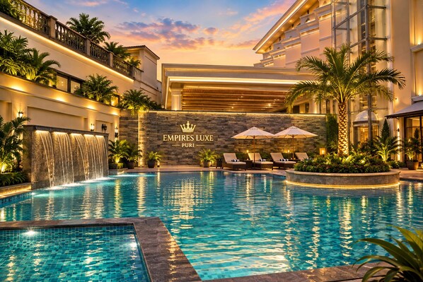 Ett poolområde vid hotellet med en vattenfallsdekoration, solstolar och en stenmur med hotellets namn.