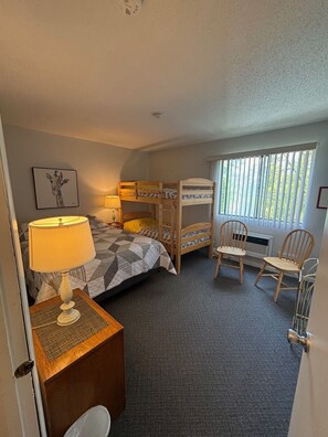 Ein Zimmer mit Etagenbetten, einem Schreibtisch mit Lampe, einem Stuhl und einem Fenster mit Jalousien.
