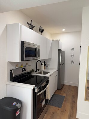 A compact kitchen with a microwave, stove, sink, and refrigerator. - Cozy 1-bedrm apartment with AC in vibrant Miami near Wynwood & Design District! (Miami)