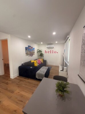A living room with a dark blue sofa, a small table with a plant, and a wall-mounted air conditioner. - Cozy 1-bedrm apartment with AC in vibrant Miami near Wynwood & Design District! (Miami)