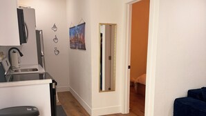A modern kitchen with a sink, refrigerator, and a trash bin. There is a hallway leading to another room with a door and a blue couch. - Cozy 1-bedrm apartment with AC in vibrant Miami near Wynwood & Design District! (Miami)
