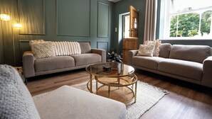 Uma sala de estar com dois sofás, uma mesa de centro e uma janela com cortinas.