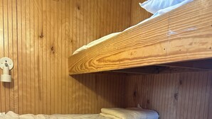 Kerrossänky, jossa on puinen pääty, yöpöytä, jossa on yksi laatikko, ja seinään kiinnitetty valaisin.