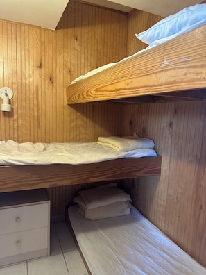 Ein Stockbett mit Holzkopfstück, ein Nachttisch mit Schublade und eine Wandleuchte.