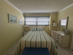Un dormitorio con cama, mesitas de noche, cómoda, ventana con persianas y techo con textura.