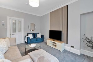 Ein modernes Wohnzimmer mit Sofa, Couchtisch, Fernseher auf einem Schrank, einer Tür und einer Wandtafel.