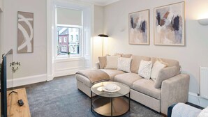 A living room with a beige sofa, a glass coffee table, and artwork on the wall. - Spacious 3BR Hawick Apartment, Sleeps 6, Parking (Scottish Borders)