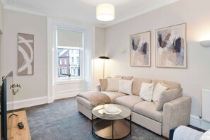 Ein Wohnzimmer mit einem beigen Sofa, einem Glastisch und Kunstwerken an der Wand.